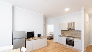 A modern kitchen with a refrigerator, oven, and sink. There is a dining table with chairs and a television on a stand. - Sea View Apartment (Margherita di Savoia)