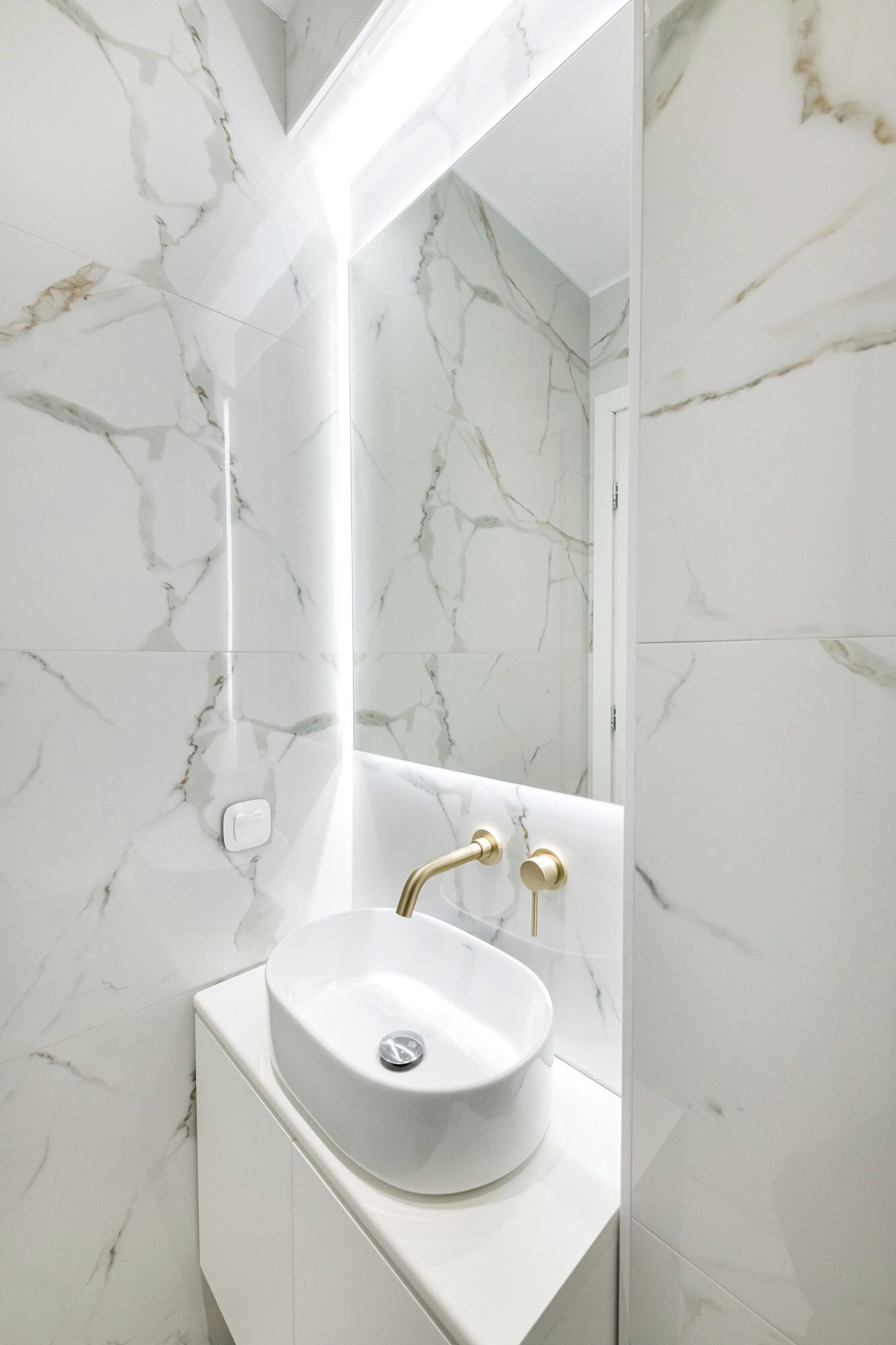Une salle de bain avec un lavabo en marbre blanc, des robinetteries dorées et un grand miroir.