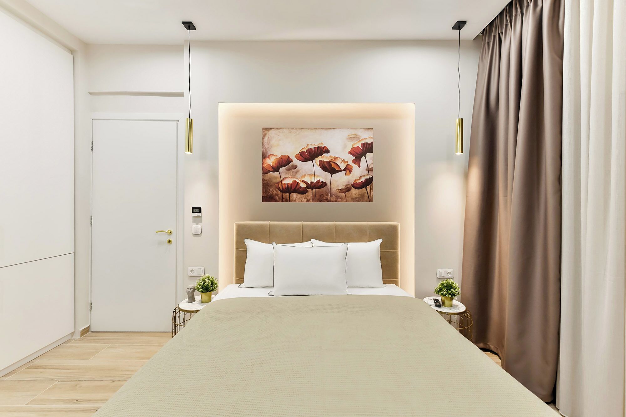 Un dormitorio moderno con una cama grande, un cabecero con un cuadro, mesitas de noche con lámparas y una puerta.