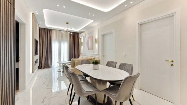 A modern dining area with a round table, grey upholstered chairs, and a marble floor. - Portoseaview Modern Luxury Apartment 131 (Thessaloniki)