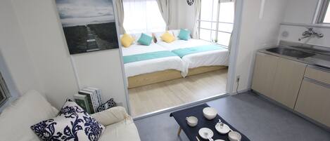 Een kleine kamer met een bed, een eettafel met borden en stokjes, een wastafel en uitzicht op een strand door het raam.