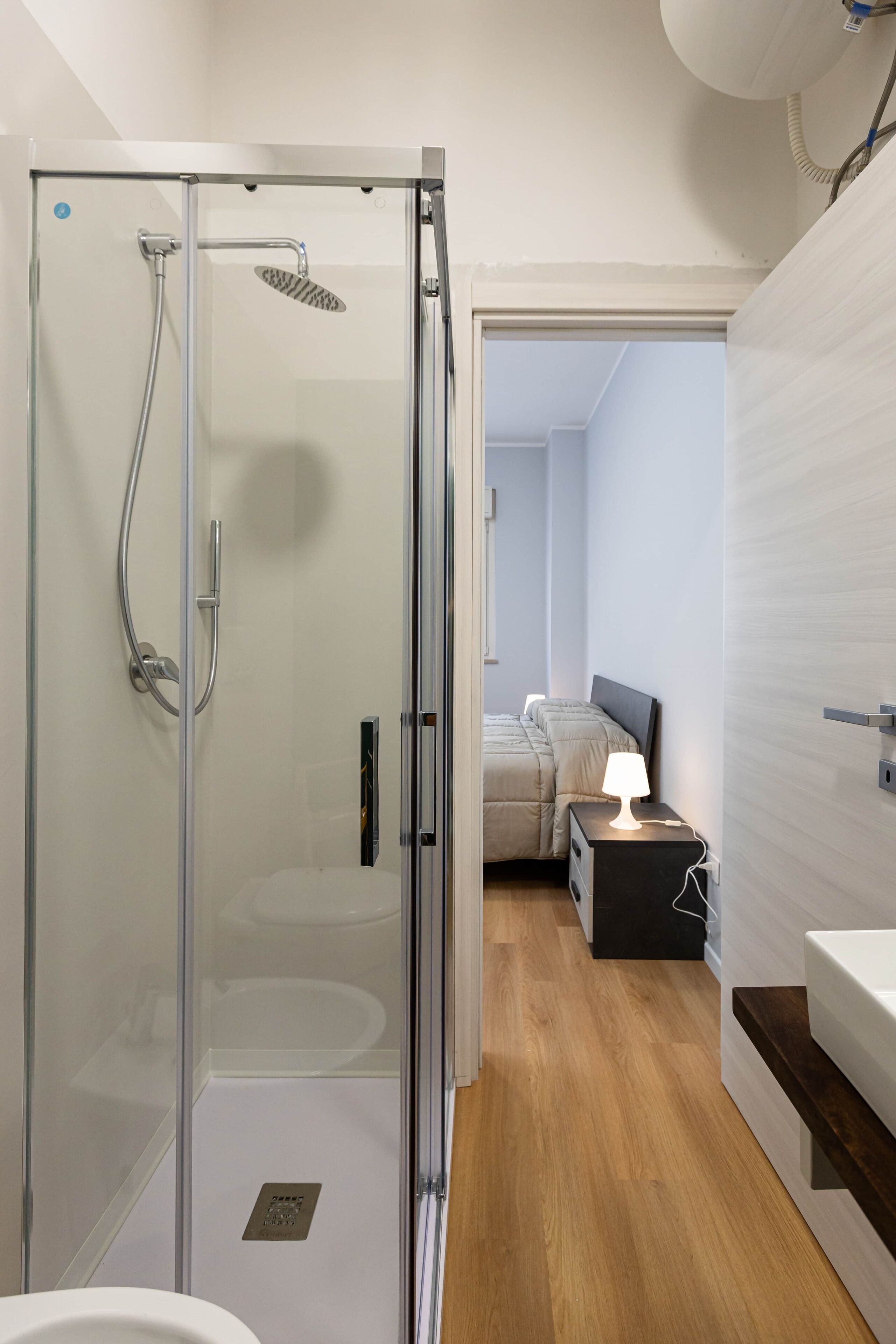 Une salle de bain moderne avec une douche à parois de verre, un lavabo blanc et une table de chevet avec une lampe.