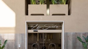 A hotel entrance with a sign reading "Hotel Suite," featuring a modern design with a glass door and potted plants on either side. - Sea View Apartment (Margherita di Savoia)