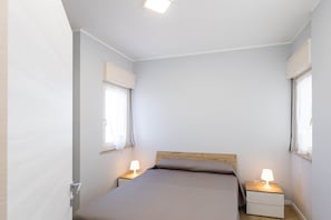 Un dormitorio con una cama individual, dos mesitas de noche con lámparas y una ventana en una pared.