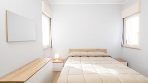 Ein schlicht eingerichtetes Schlafzimmer mit Bett, Nachttischen und einer Wandlampe.