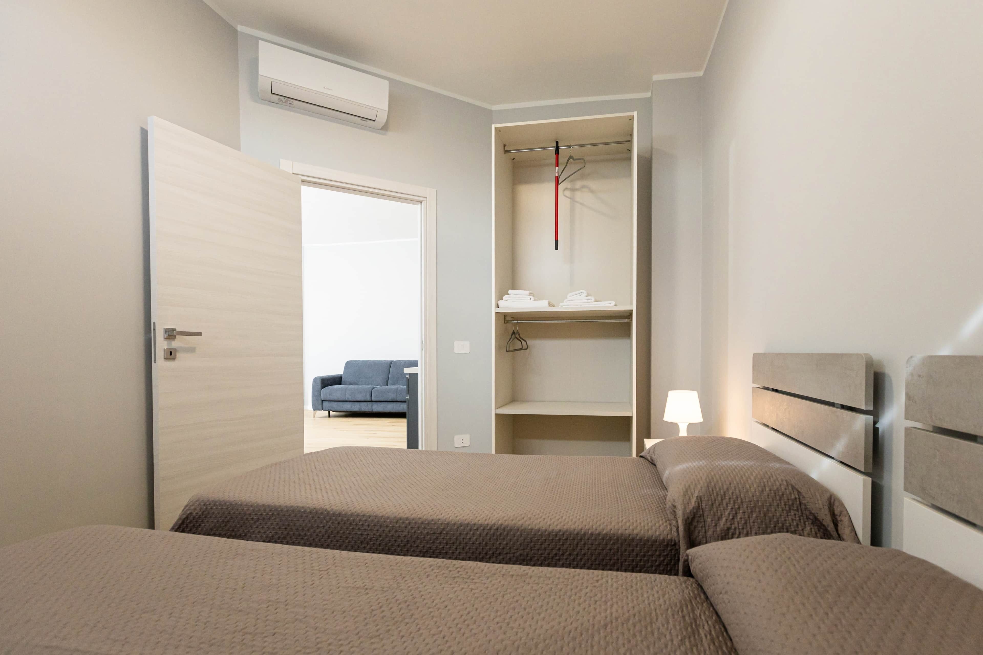 Ein Hotelzimmer mit zwei Betten, einem Kleiderschrank mit Kleidung und einem blauen Stuhl im Hintergrund.