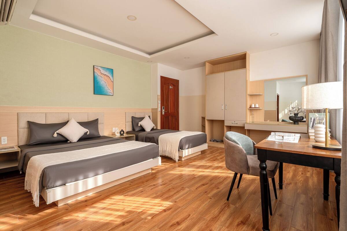 Habitación de hotel con dos camas, un escritorio, una silla, un espejo y una puerta.