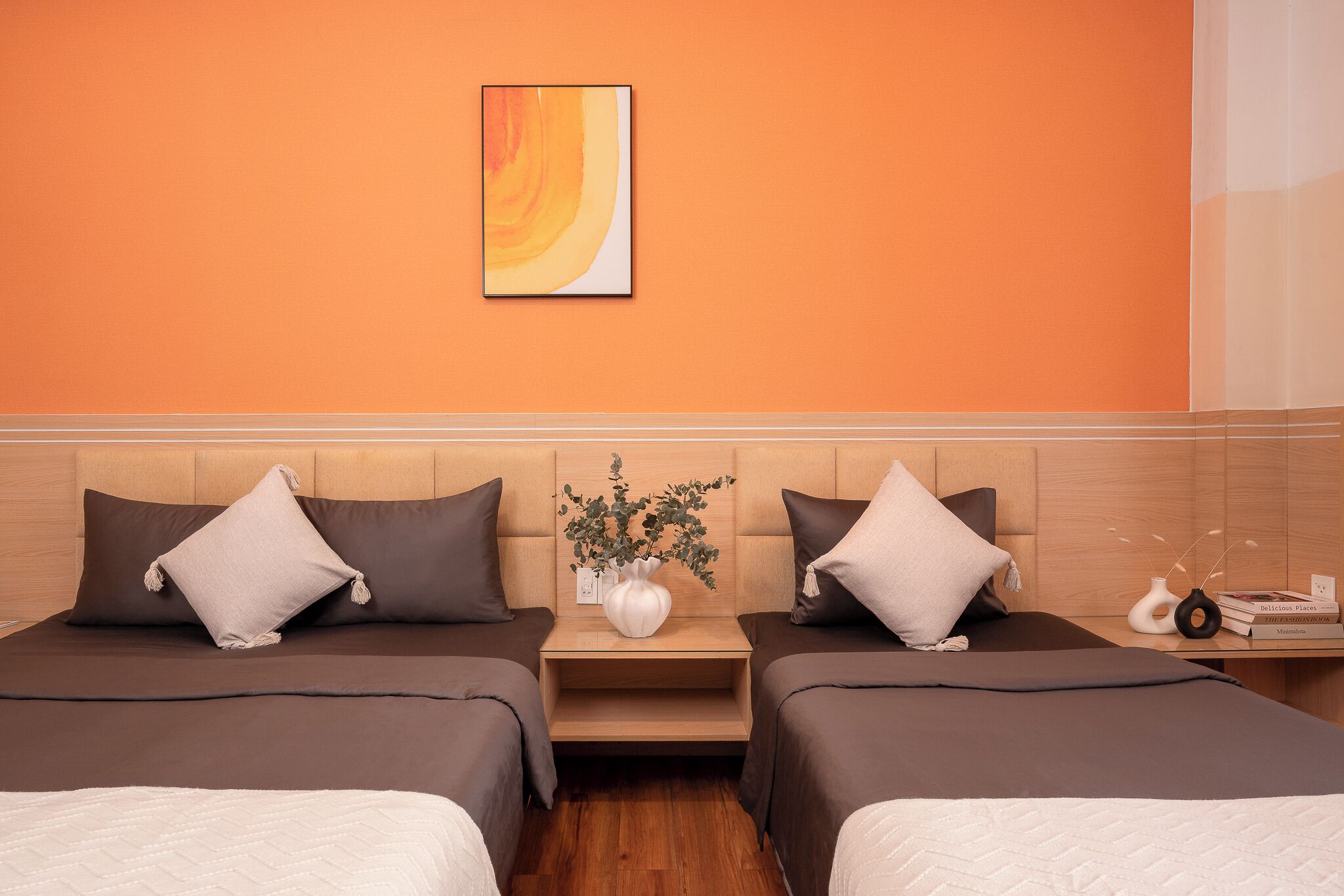 Habitación de hotel con dos camas, cabecero de madera, un florero con flores y un cuadro en la pared.