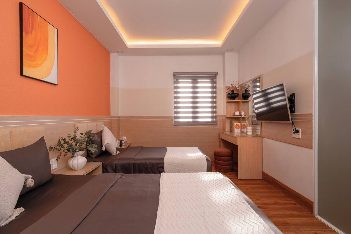 Una habitación de hotel moderna con dos camas, un televisor, un escritorio pequeño y una ventana con persianas.