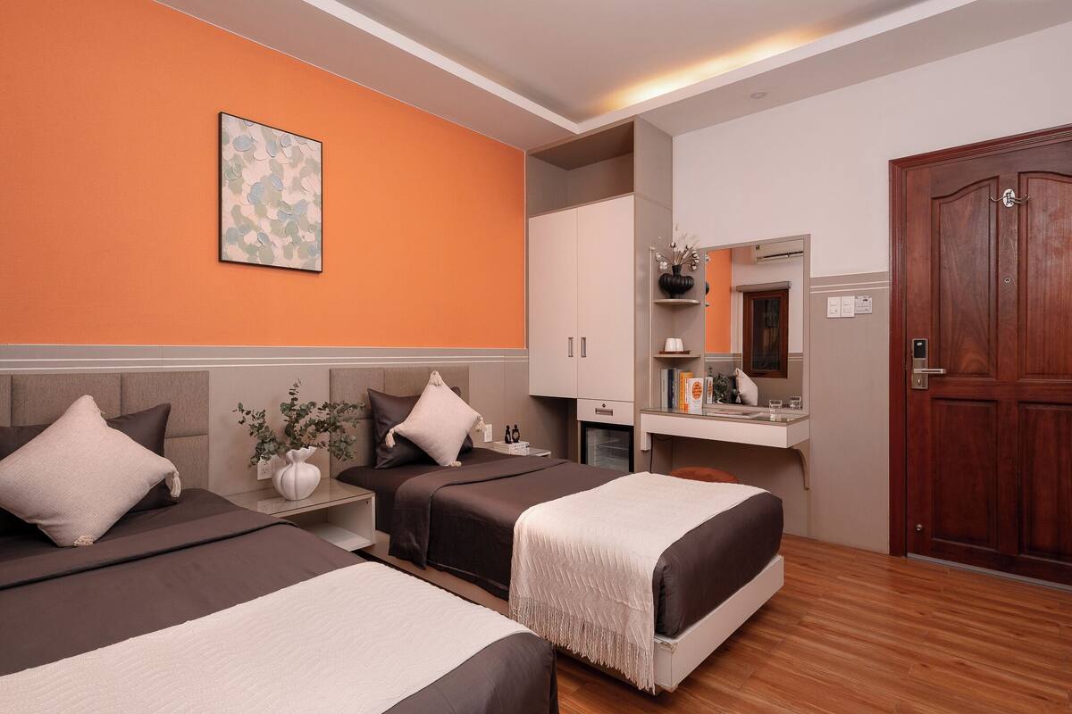Una habitación de hotel con dos camas, un tocador con espejo y una puerta de madera.
