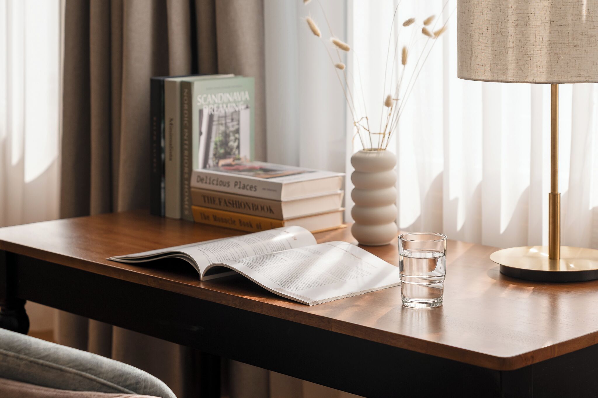 Un bureau en bois avec un livre, un verre d’eau et une lampe.