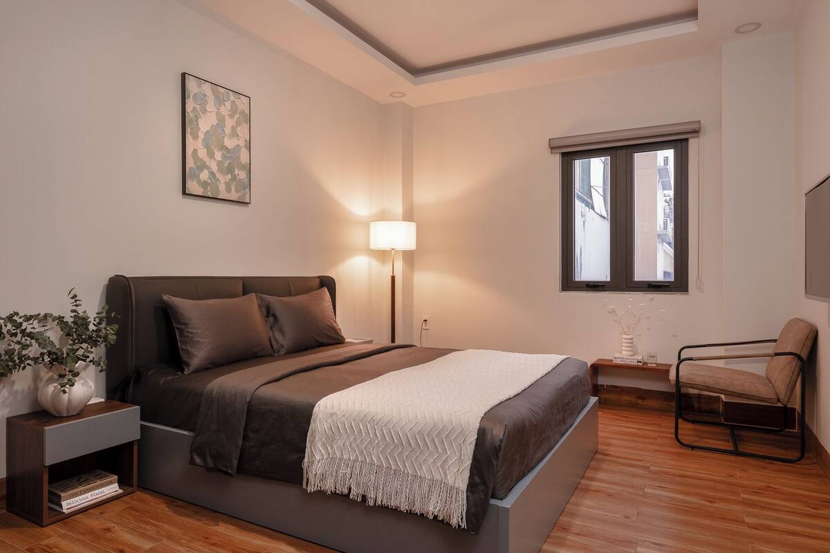 Un dormitorio moderno con cama, mesita de noche, lámpara, silla y una obra de arte en la pared.