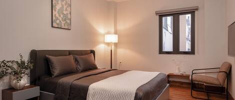 A modern bedroom with a bed, bedside table, lamp, chair, and artwork on the wall.