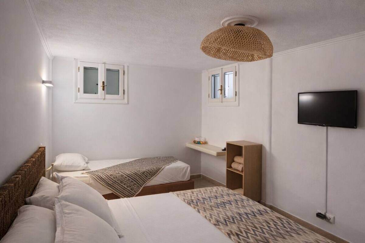 A bedroom with two beds, a television, a shelf, and a ceiling lamp.