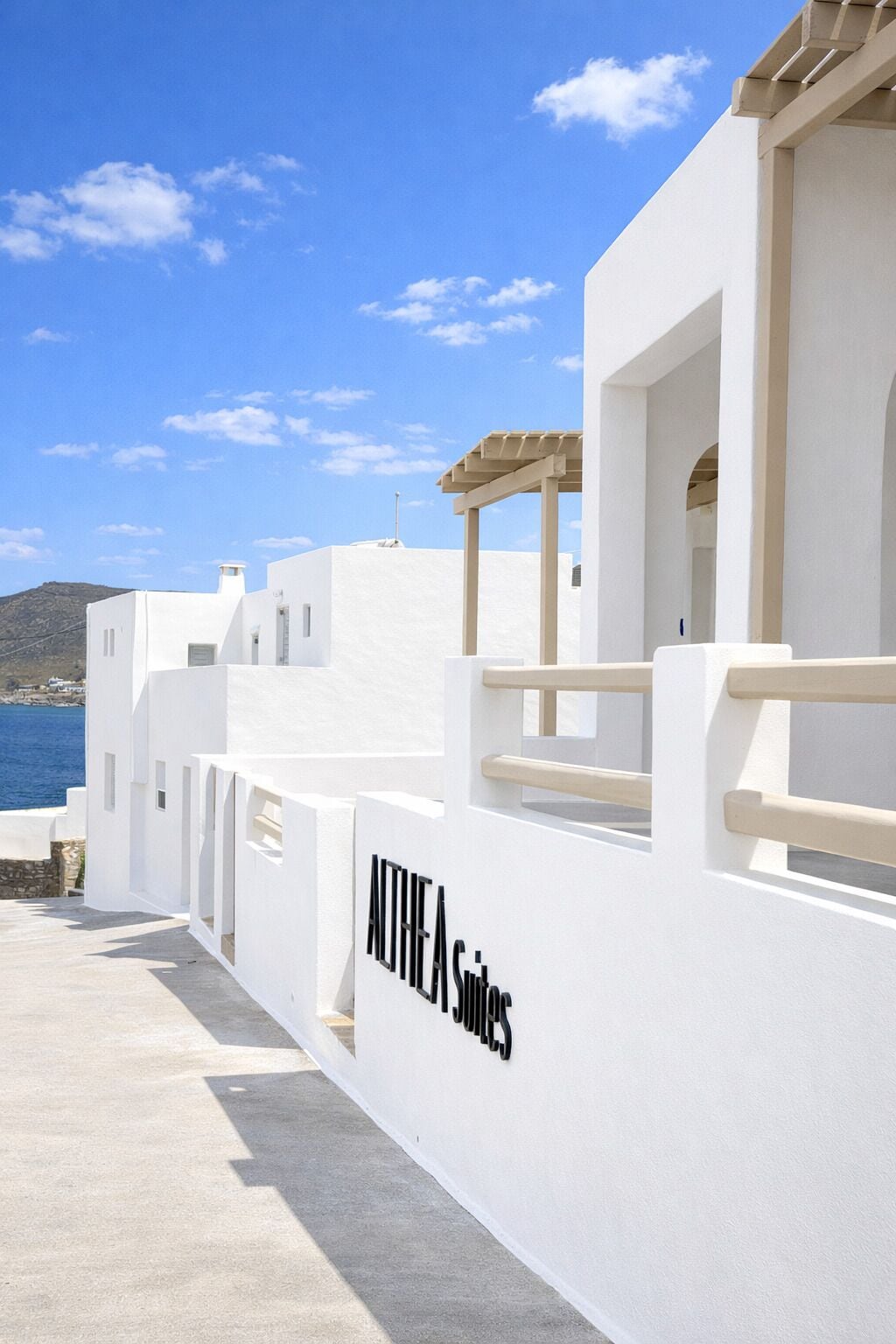 A white building with a sign reading 'ANTHEA Suites' and a view of the sea.