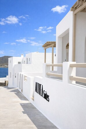 A white building with a sign reading 'ANTHEA Suites' and a view of the sea.