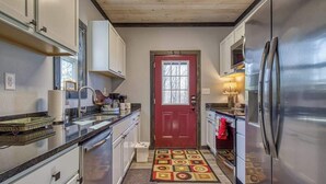 A compact kitchen with stainless steel appliances, white cabinetry, and a red door. - Sassy Bear Hideaway by Beyond Expectations: 4BR w/ Firepit, Game Room & Hot Tub (Sevierville)