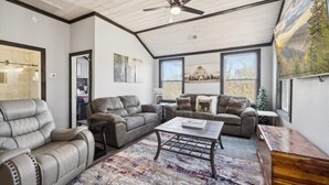 A spacious living room with leather sofas, a coffee table, and large windows offering views of the outdoors. - Sassy Bear Hideaway by Beyond Expectations: 4BR w/ Firepit, Game Room & Hot Tub (Sevierville)