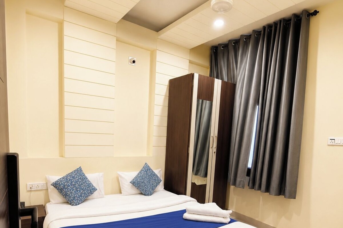 A hotel room with a large bed, a wardrobe, a ceiling fan, and a window with curtains.
