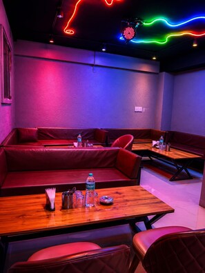 A dimly lit room with red seating and tables, neon lights on the ceiling, and a water bottle on the table. - Hotel Shreenathji Inn (Udaipur)