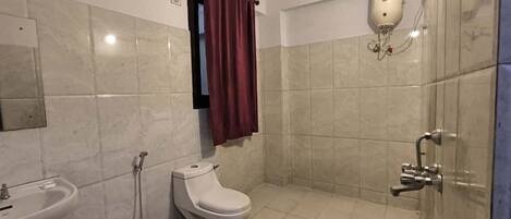 A bathroom with a toilet, sink, shower, and a bucket.
