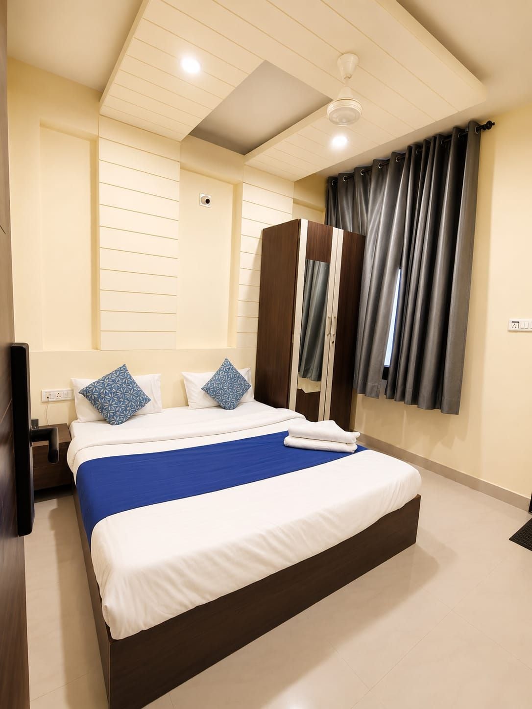 Een hotelkamer met een groot bed, een kledingkast, een plafondventilator en een raam met gordijnen.