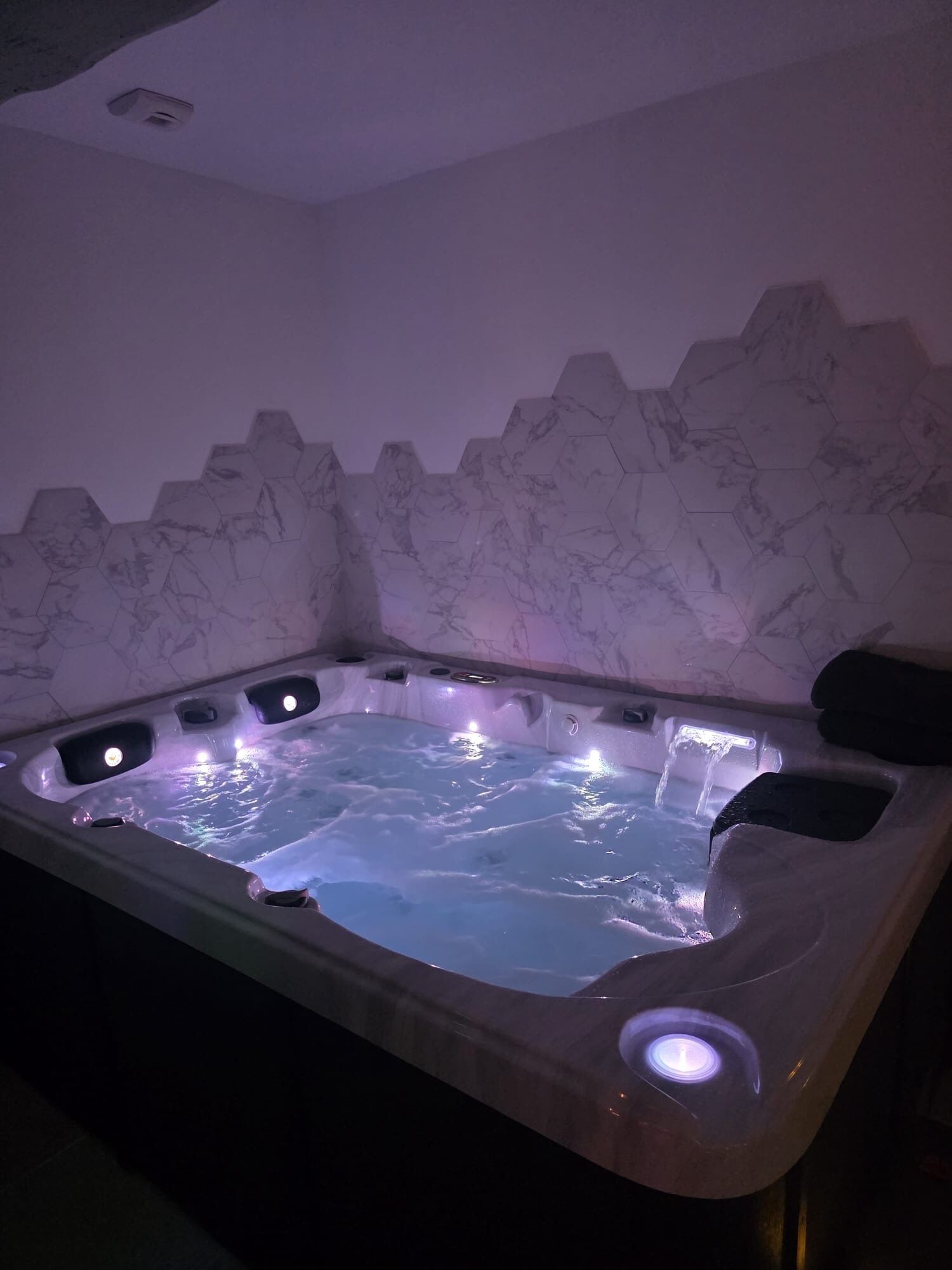 Een bubbelbad met een achtergrond van marmeren wanden en een plafondlamp.