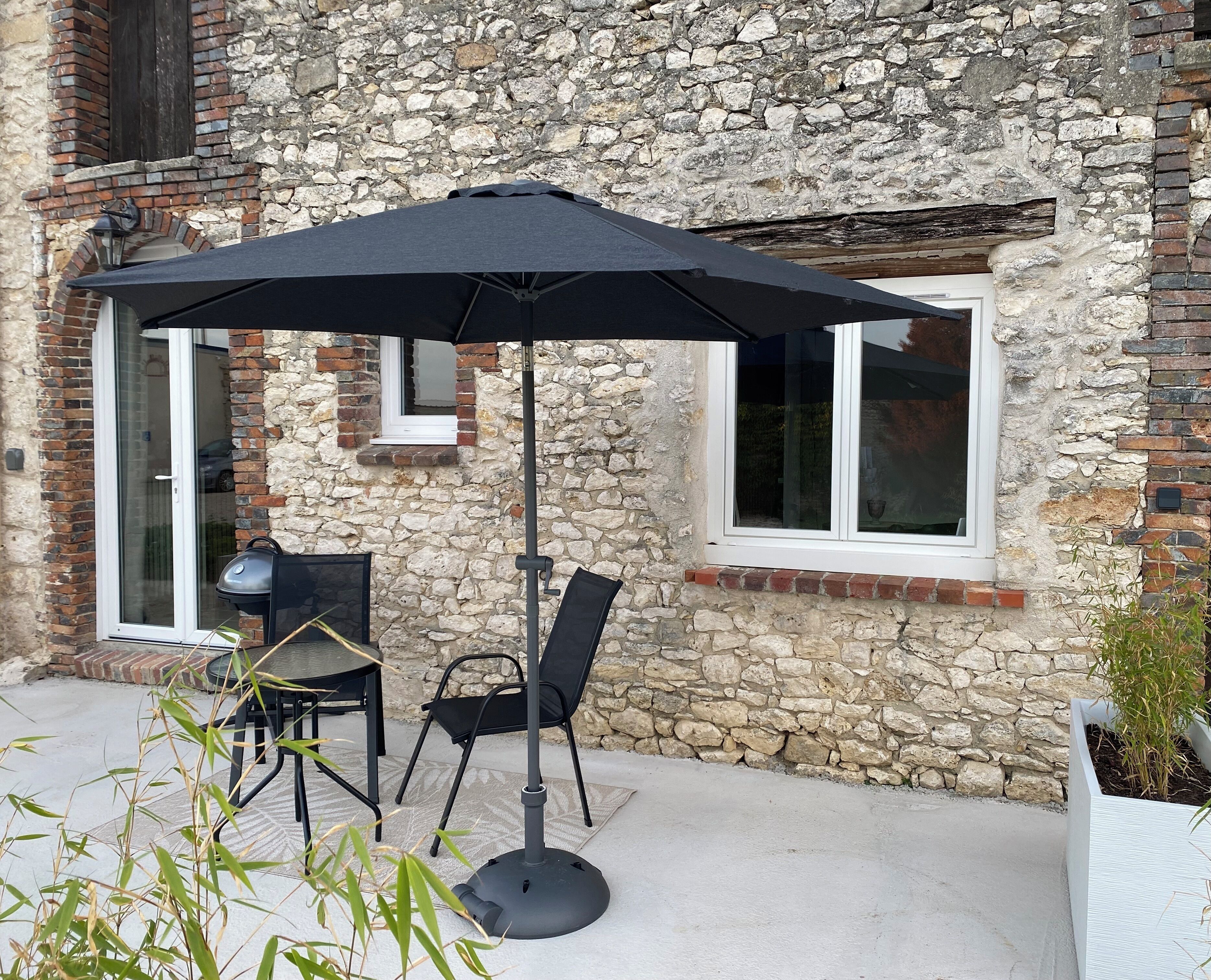 An outdoor patio with a table and chairs, a black umbrella, and a stone wall.