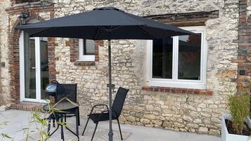 An outdoor patio with a table and chairs, a black umbrella, and a stone wall.