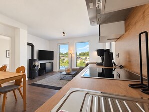 A modern kitchen with a built-in stove, a dining area with a wooden table and chairs, and a large window offering a view of the outdoors. - Spacious Apartment with Exceptional Mountain View, Sauna and Terrace (Winterberg)
