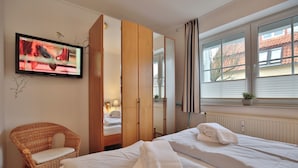 Ett hotellrum med två sängar, en tv, en fåtölj i rotting och ett fönster med utsikt över byggnader.