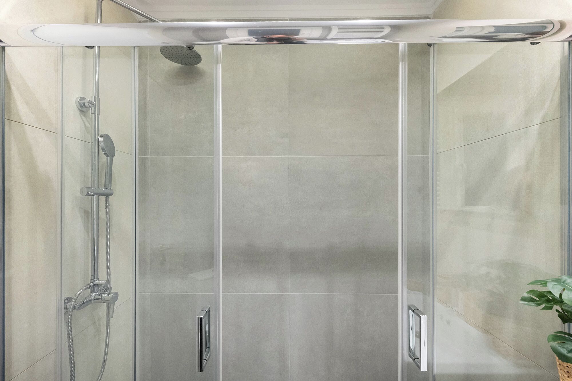 A modern shower enclosure with a glass door, a handheld showerhead, and a wall-mounted faucet.