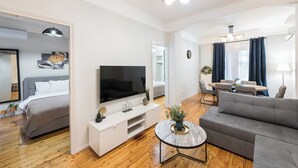 Een moderne woonkamer met een flatscreen televisie, een bank, een salontafel en een eethoek met een tafel en stoelen.