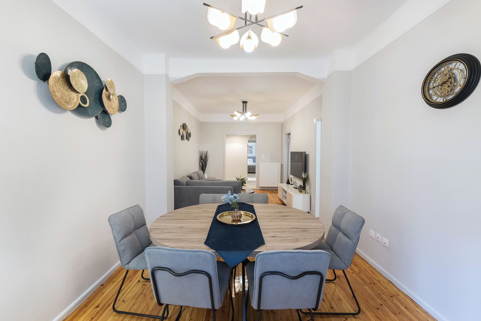 Un comedor moderno con una mesa redonda de madera, cuatro sillas grises tapizadas y una araña.