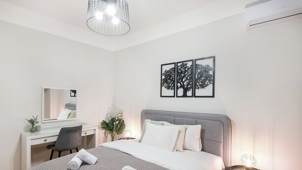 Een moderne slaapkamer met een bed, nachtkastje, lamp en een bureau met stoel.