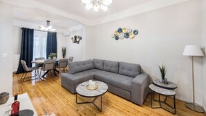 Een moderne woonkamer met een grijze hoekbank, twee ronde salontafels, een eethoek met een tafel en stoelen, en decoratieve muurkunst.