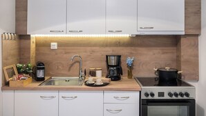 Een moderne keuken met witte kastjes, een roestvrijstalen spoelbak, een koffiezetapparaat, een waterkoker en een fornuis.