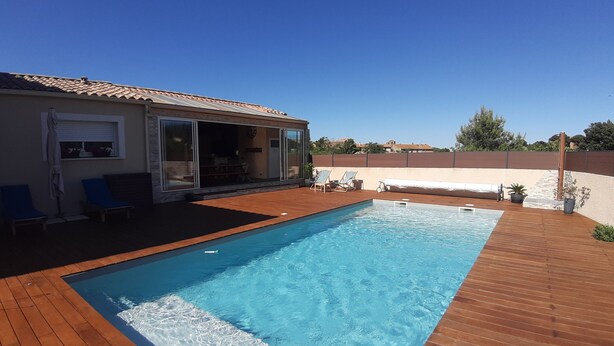 A swimming pool with a wooden deck, a covered patio, and a sliding glass door leading to an interior space. - Comfortable villa between the Mediterranean and the Corbières (Boutenac)