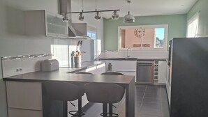 A modern kitchen with a central island, bar stools, and a large refrigerator. - Comfortable villa between the Mediterranean and the Corbières (Boutenac)