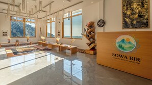 A spacious room with large windows, a wooden reception desk, and a wall-mounted decorative piece.