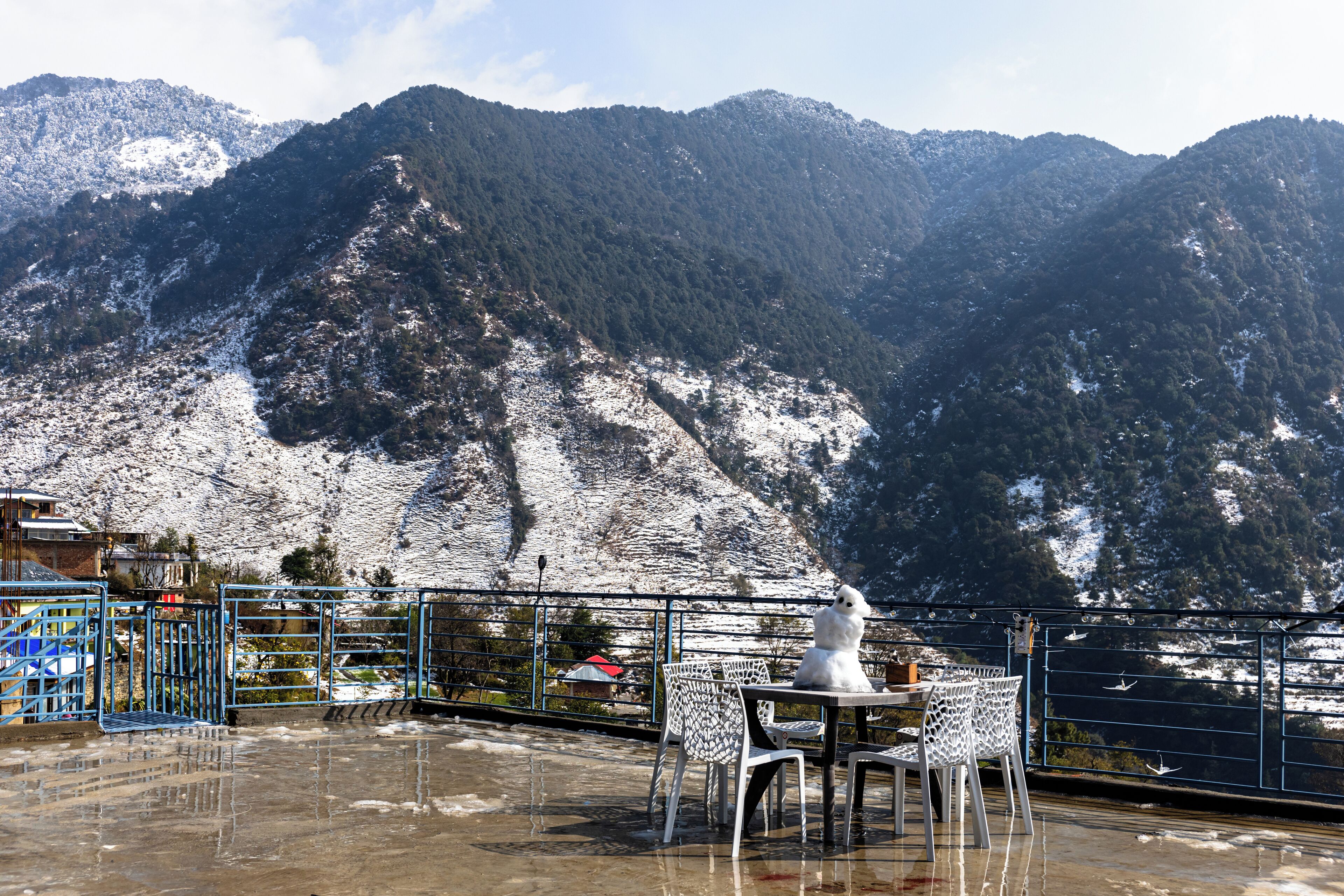 Una terraza con mesa y sillas que ofrece vistas a un paisaje montañoso con parches de nieve.