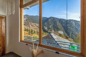 A room with a large window offering a view of a mountainous landscape. - Sowa Stays Bir (Baijnath)