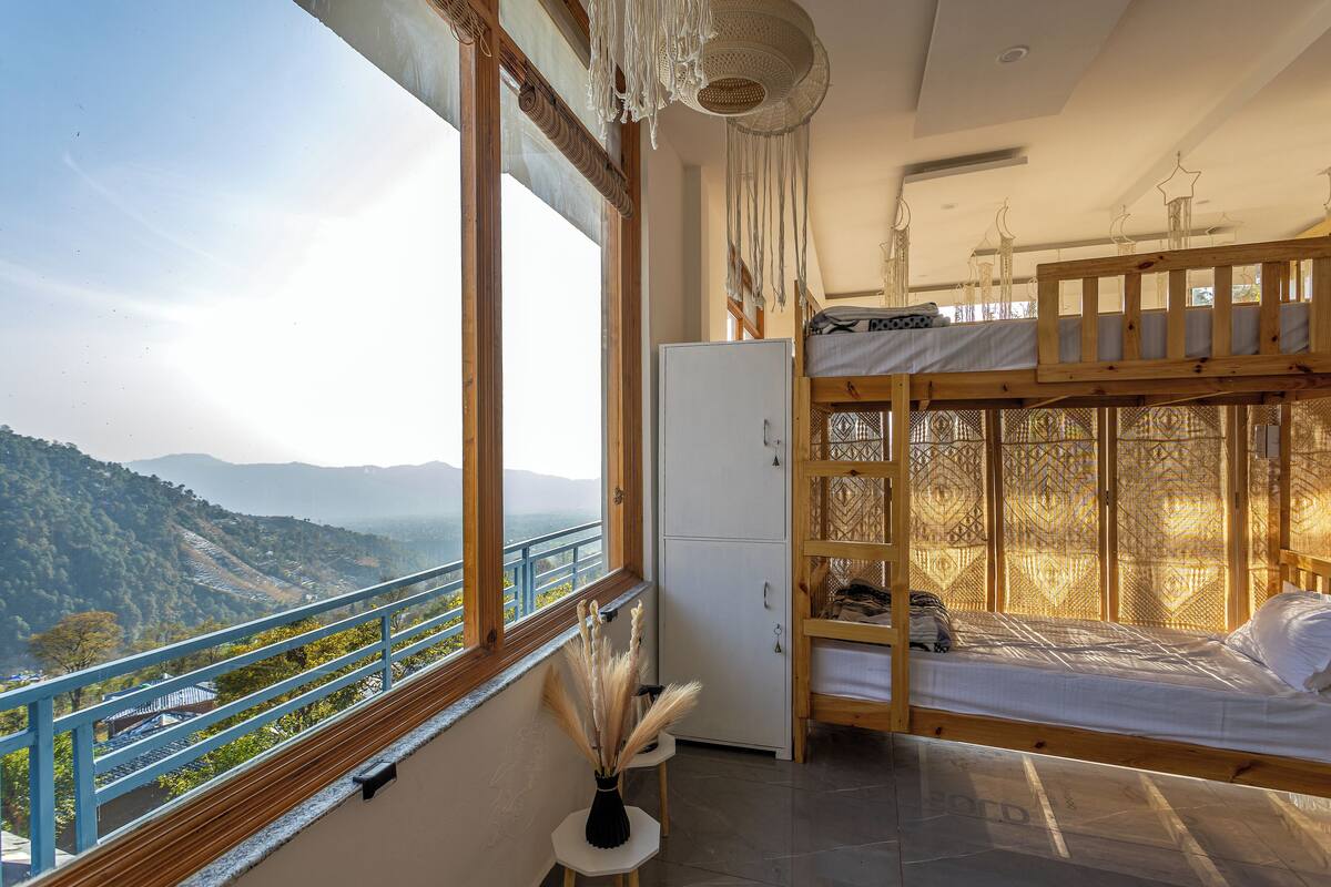 A room with a bunk bed, a white refrigerator, and a view of a mountainous landscape through a large window.