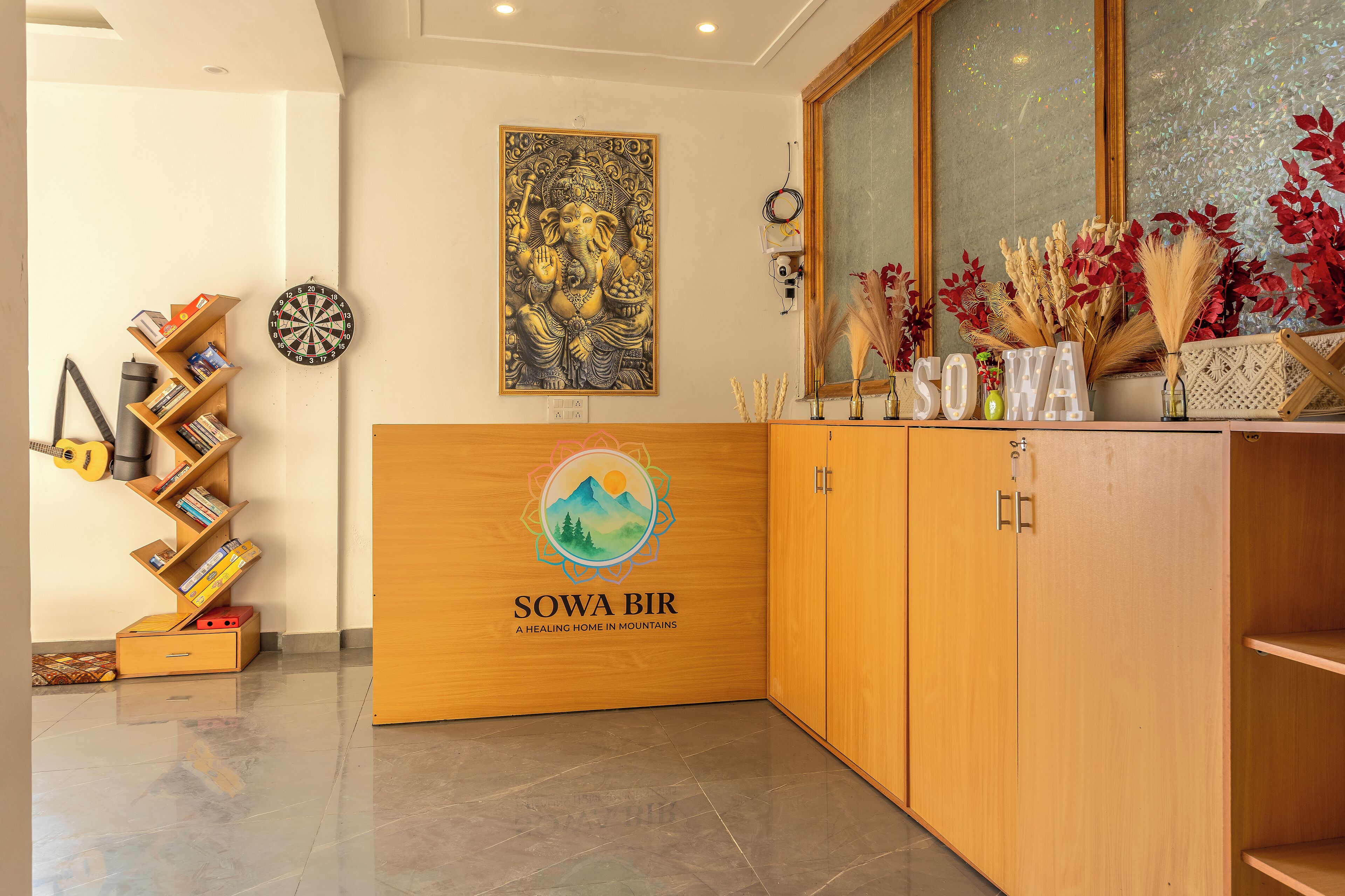 Um quarto com um armário de madeira, um alvo de dardos, uma estante e uma parede com um quadro emoldurado e o logotipo da 'Sowa Bir'.