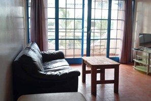 A room with a black leather sofa, a wooden table, and a TV on a stand. - Peaceful apartment in Saly, a stone's throw from the sea (Saly)