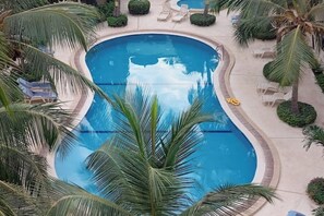 A large, oval-shaped swimming pool surrounded by palm trees and lounge chairs. - Peaceful apartment in Saly, a stone's throw from the sea (Saly)