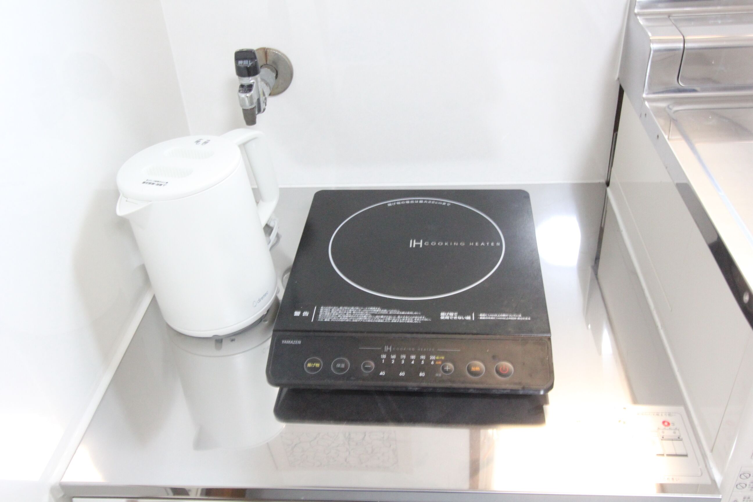 Una cocina moderna con un calentador IH integrado, una cafetera blanca y una encimera de acero inoxidable.