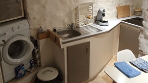 A compact kitchen with a washing machine, sink, and a small table with a blue towel. - Charming studio, suspended time, pets welcome (Malaucène)