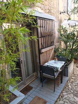 A small outdoor seating area with a table and chairs, surrounded by plants and a stone wall.