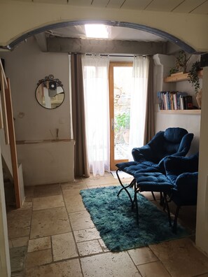 A room with a blue armchair, a mirror, a bookshelf, and a view through a door.